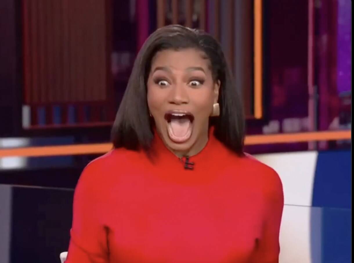 Woman in a red top on a TV set, mouth wide open in surprised/excited expression.