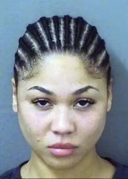 Mugshot-style photo of a young woman with tightly braided hair pulled back, neutral expression, wearing a dark top against a gray background.