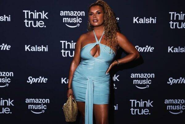 Woman in a light-blue halter mini dress posing on a dark backdrop with sponsor logos.