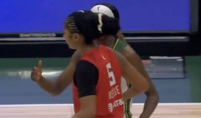 Two basketball players on an indoor court; red jersey with number 5 gestures with a thumbs up while a teammate in green stands behind them.
