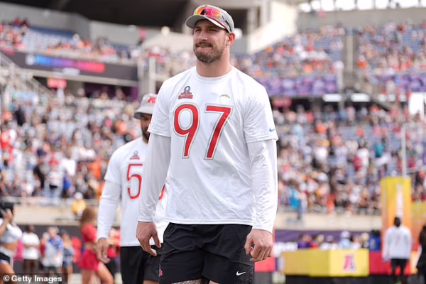 Male athlete in a white jersey with the number 97 walks on a sports field as fans watch from crowded stands behind him.