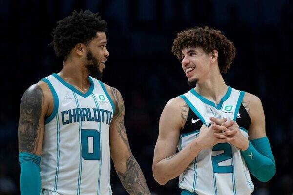 Two Charlotte Hornets players in white-teal uniforms smile and chat on the court during a game, number 0 and number 2 visible on their jerseys.
