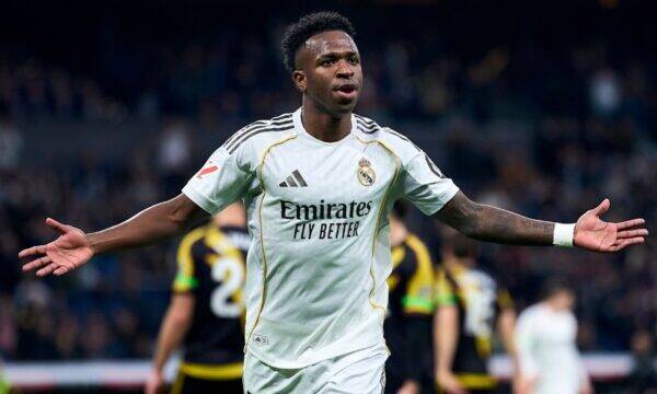 Soccer player in a white Real Madrid jersey with arms outstretched, celebrating on the pitch.