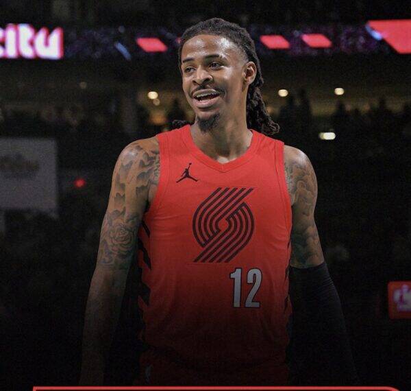 Basketball player in a red jersey with number 12, smiling on a dimly lit court.