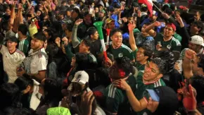 Crowd of soccer fans cheering in green jerseys, arms raised, at a game.