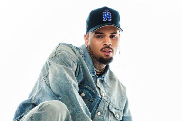 Man wearing a faded blue denim jacket and a black cap with a blue LA logo, posing against a white background.