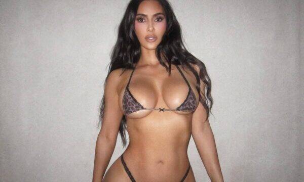 Woman in a leopard-print bikini posing against a gray wall.
