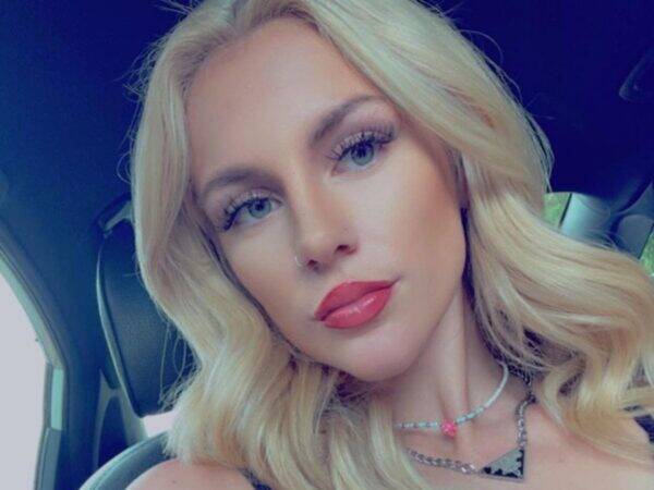 Close-up portrait of a young woman with blonde hair and pink lipstick inside a car