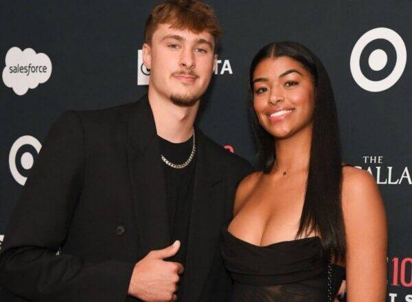 Two people pose together on a red carpet, smiling, with a dark backdrop featuring logos in the background (salesforce, Target). They wear black outfits.
