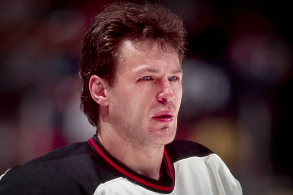 Hockey player with a bleeding lip and stubble, wearing a black and white jersey with a red collar, looking off to the side.