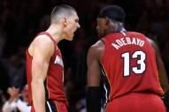 Two basketball players in red jerseys argue on the court during a game, with the number 13 visible on the back of one player's jersey.