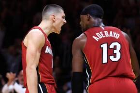 Two basketball players in red jerseys argue on the court during a game, with the number 13 visible on the back of one player's jersey.