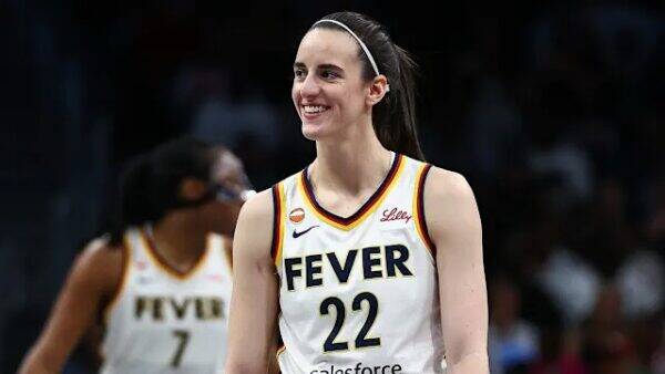 Female basketball player in a Fever jersey #22 smiling on the court, with a teammate in the background.