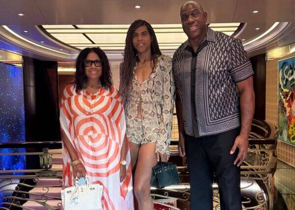Three adults pose together on a railing indoors; left woman in orange-white swirled dress with white bag, middle woman in snakeskin-print outfit with shorts and green handbag, man on right in geometric patterned shirt and black pants.