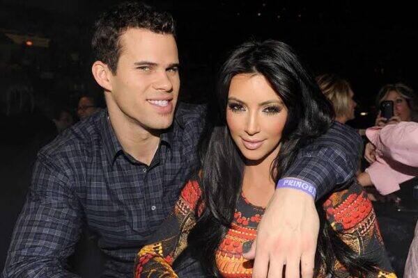 Couple posing for a photo at a night event: man in a dark plaid shirt and woman with long dark hair in a patterned top, arm around each other.