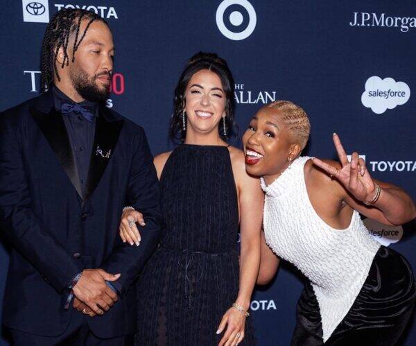 Three people posing on a blue carpet at a formal event, smiling for the camera with two women and a man in evening wear close together.