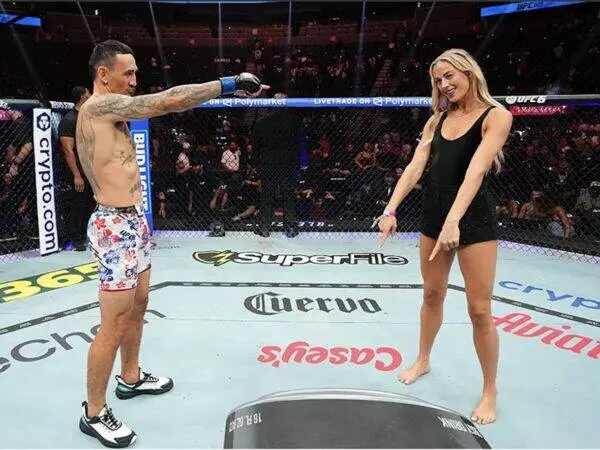 Two people stand in a UFC octagon facing each other; man points toward a woman in a black dress as spectators watch.