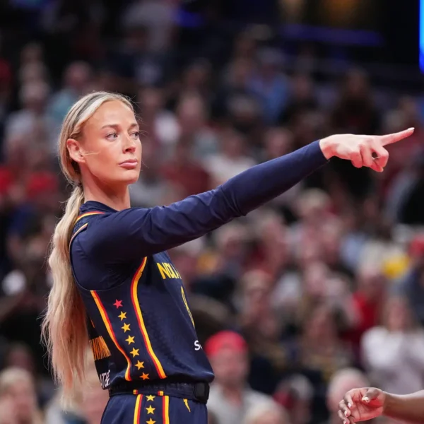 Female athlete in a navy Netherlands uniform with red-yellow trim points to the right during a game, crowd blurred in the background.