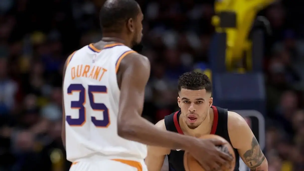 Basketball action: player in a white Durant 35 jersey guards the ball against a defender in a dark jersey on the court.