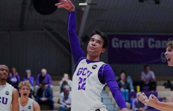 Basketball player in a white jersey with purple sleeves (#22) leaps with arm raised during a game, crowd in the background.
