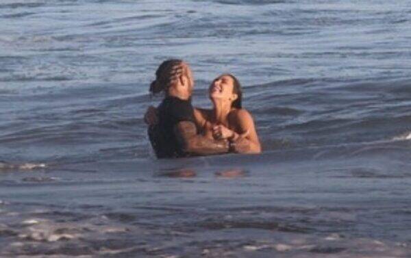 Two people standing waist-deep in the ocean embrace each other in the surf, facing and leaning toward one another.