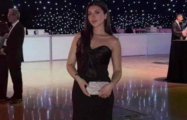 Woman in a strapless black evening gown holding a silver clutch at a formal event on a lit dance floor.