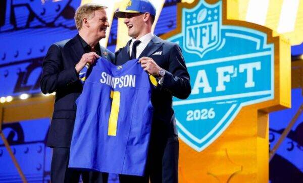 Two men in suits on stage hold up a blue jersey that reads 'Simpson' with the number 1 at the 2026 NFL Draft event.