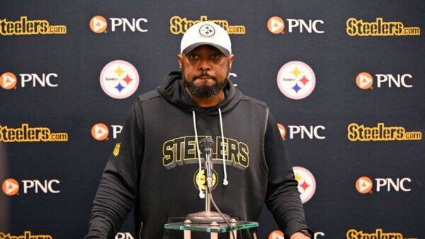 Man in a Steelers hoodie at a press conference podium, microphone in front, backdrop with Steelers and PNC logos behind him.