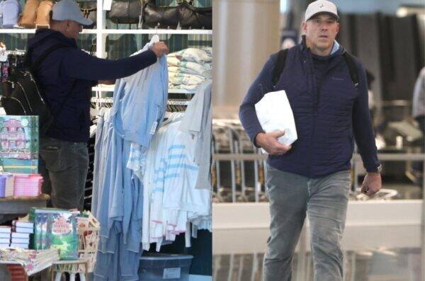 Two men in navy vests shop: left man selects light-blue jackets from a rack; right man walks carrying a white paper bag.