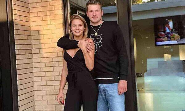 Couple posing together outside a brick storefront, the man's arm around the woman's shoulders as they smile at the camera.