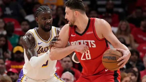 Rockets guard in red drives with the ball as a Lakers defender in white and purple closely guards him.