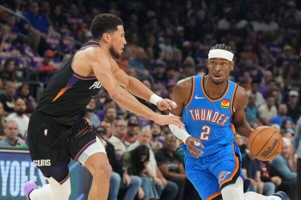 Thunder guard (number 2) dribbles the ball past a Suns defender during an NBA game with a crowded arena in the background, intense expression on both players' faces.