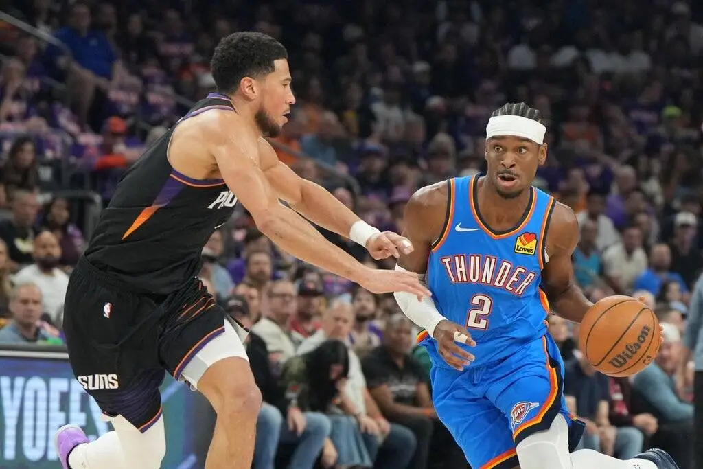 Thunder guard (number 2) dribbles the ball past a Suns defender during an NBA game with a crowded arena in the background, intense expression on both players' faces.