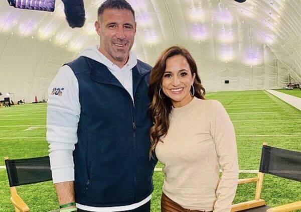 Smiling man and woman pose together inside a large indoor sports facility with artificial turf under a dome.