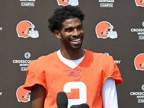 Smiling African American football player in an orange jersey (#3) at a press event with Browns logos in the background, microphones in front of him.