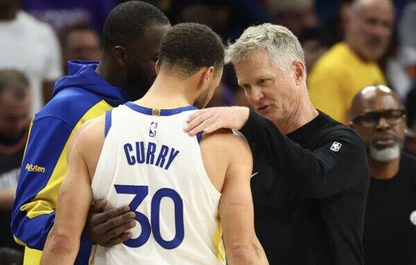 Basketball coach places a hand on a player's shoulder during a timeout, a white jersey with the number 30 visible.