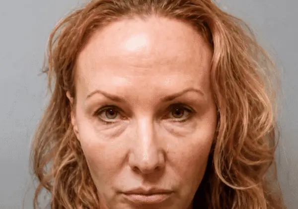 Mugshot-style portrait of a woman with reddish hair and a neutral expression against a gray background.