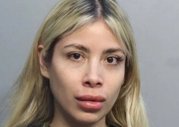 Close-up portrait of a woman with long blonde hair and a neutral expression against a gray background.