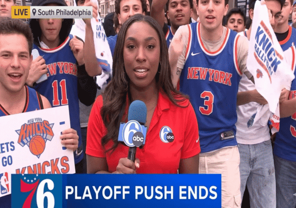 Live reporter with blue mic in front of a crowd of Knicks fans in Philadelphia, banner reads LIVE South Philadelphia (news broadcast).