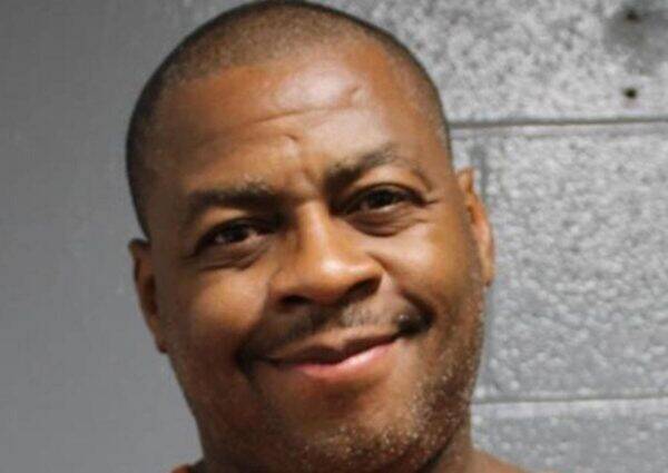 Close-up portrait of a smiling man with short hair against a gray wall background.