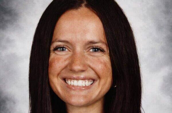 Smiling woman with long dark hair against a gray studio backdrop.