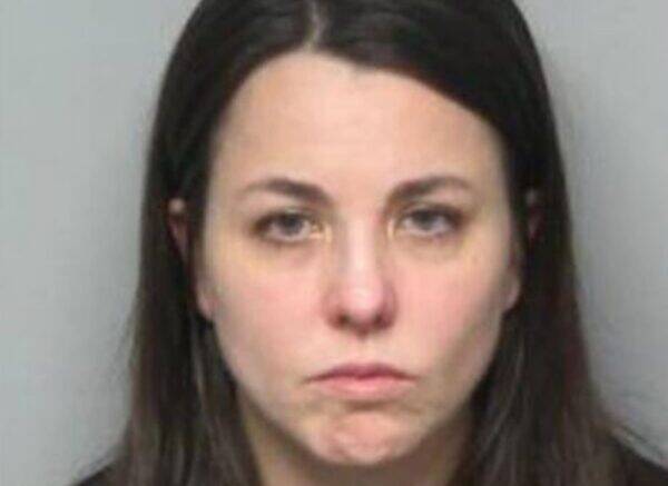 Front-facing mugshot of a woman with long dark hair and a neutral, solemn expression against a gray background.