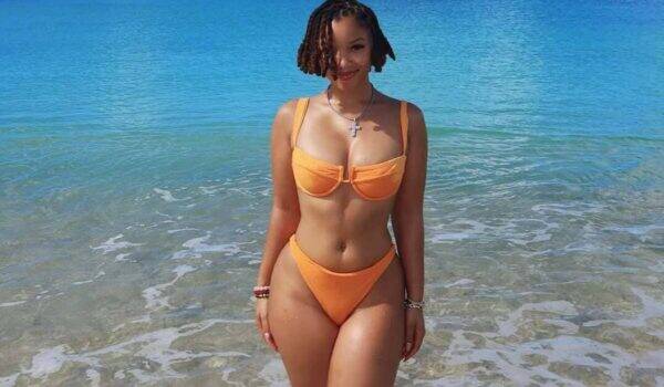 Woman in an orange bikini standing in shallow ocean water at the beach, facing the camera.