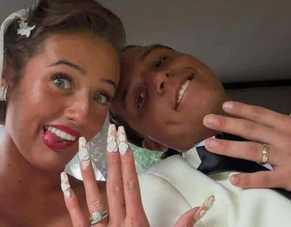 Bride and groom take a playful selfie, showing off wedding rings and the bride’s long lace nails.