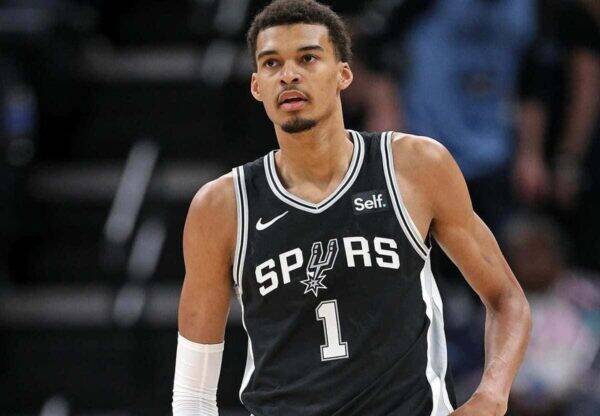 Basketball player in a Spurs black jersey with number 1, standing on the court during a game, looking ahead.