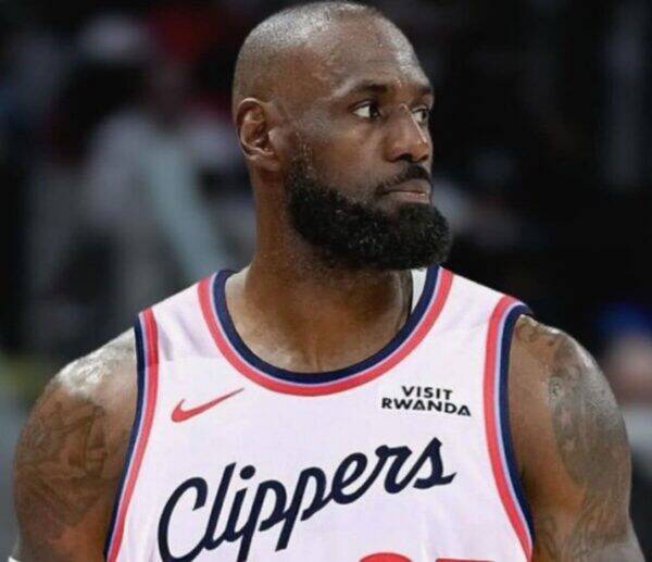 Basketball player in a white Clippers jersey with red and blue trim, looking to the right with a full beard.