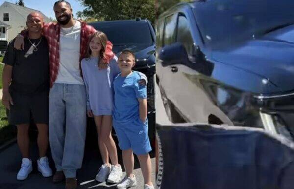 Family of four posing together outdoors in front of a black SUV on a sunny day.
