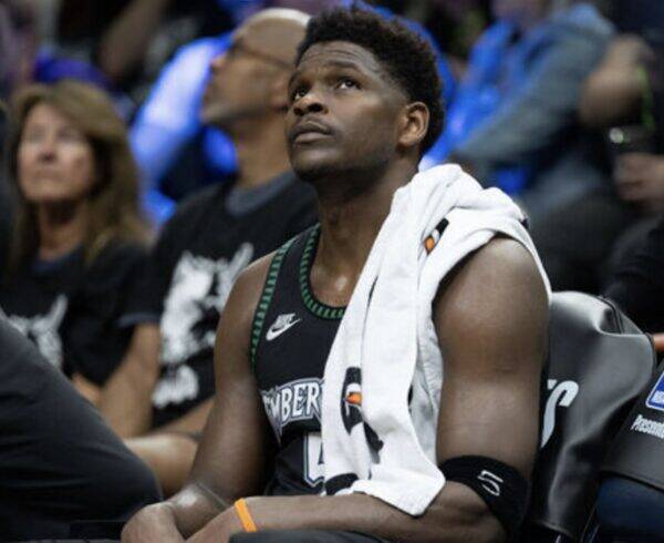Basketball player sits on a bench with a towel over his shoulder, looking up during a game.