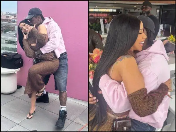Couple posing affectionately: man in a pink hoodie lifts woman in a brown knit dress against a pink wall, rooftop setting.