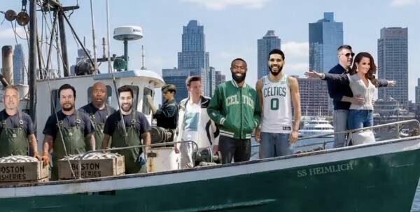 Group of men on a green fishing boat in a harbor, with a city skyline in the background.